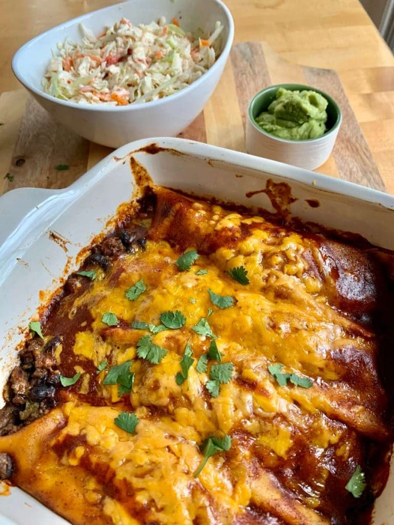 cooked gluten-free beef black bean enchiladas in a casserole with guacamole and coleslaw