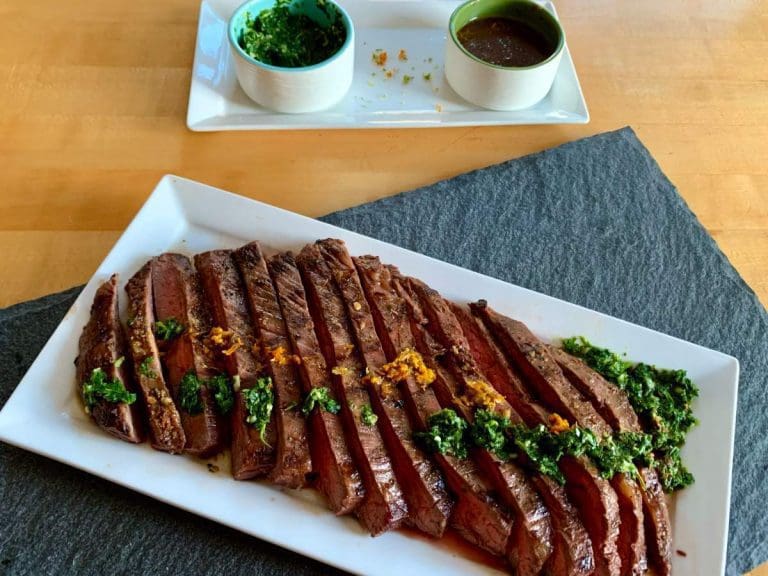 Cuban style grilled flank steak on a platter with chimichurri sauce