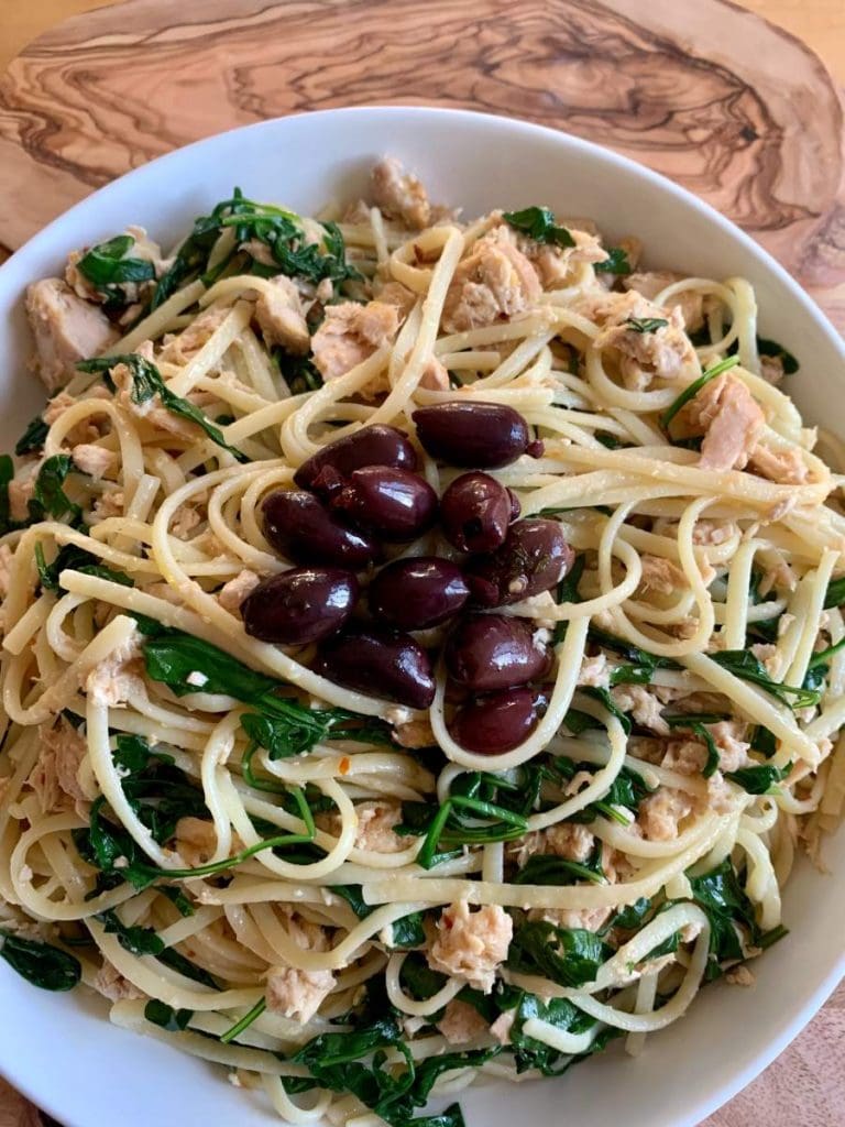 Tuna Pasta with Lemon and Arugula garnished with black olives in a white bowl
