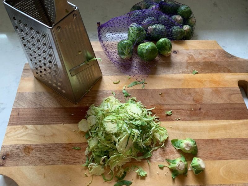 Shreded Brussels sprouts and a box grater on a cutting board